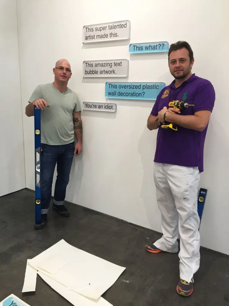 Unix Gallery's David Solomon (left) and Alex Cesaria (right) complete an install of text works by Desire Obtain Cherish. 