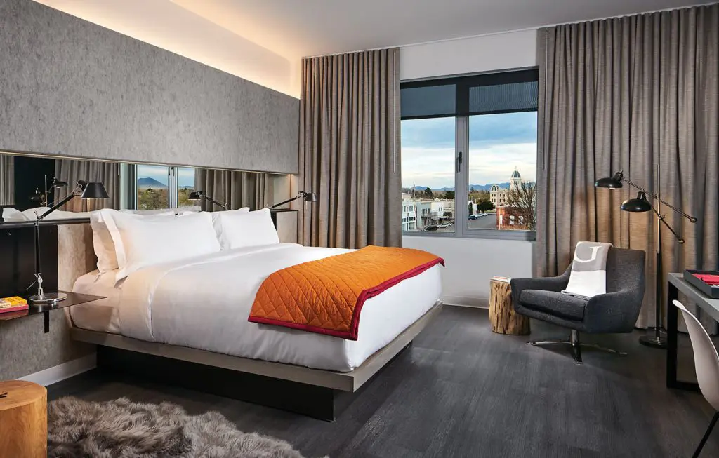 Guest rooms are extra large, with views of Marfa and the Chinati mountains beyond. Designer Alice Cottrell mixed industrial and midcentury furnishings. The orange quilted blanket was inspired by movers’ blankets used to wrap furniture for delivery.
