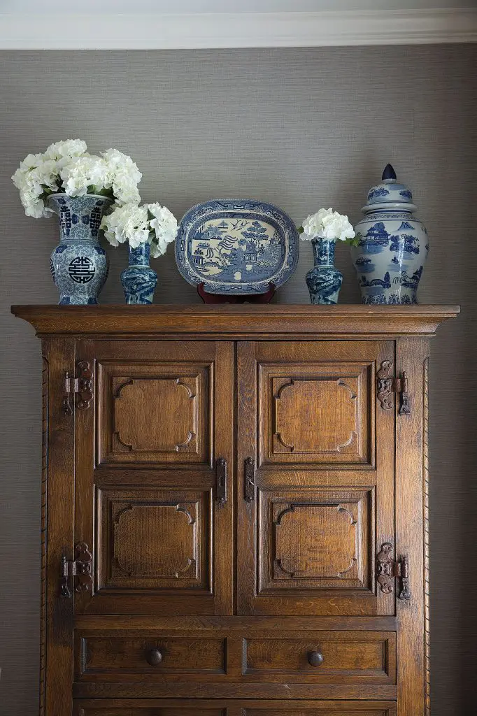 A vintage armoire provides linen storage in the dining room. Blue and white pottery sits pretty atop.