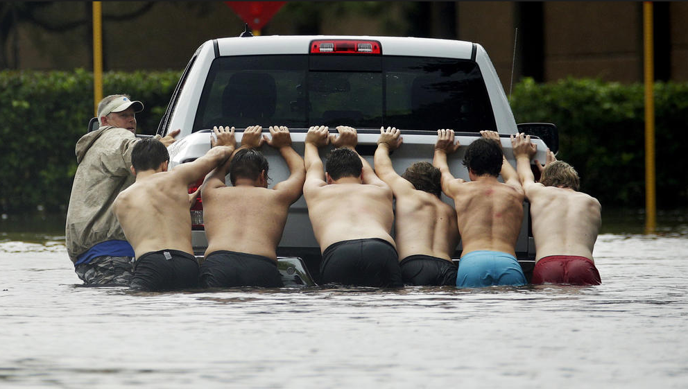Residents join together to push a stalled pick-up truck through rising flood waters. (Photo by Charlie Riedel / Associated Press) 