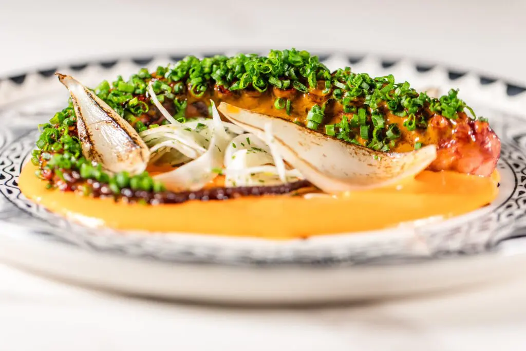 The octopus appetizer ($25) at Okto is prepared sous-vide before it’s seared and placed upon a spicy rendition of romesco sauce with chives and bruleed onions. (Photo by Becca Wright)