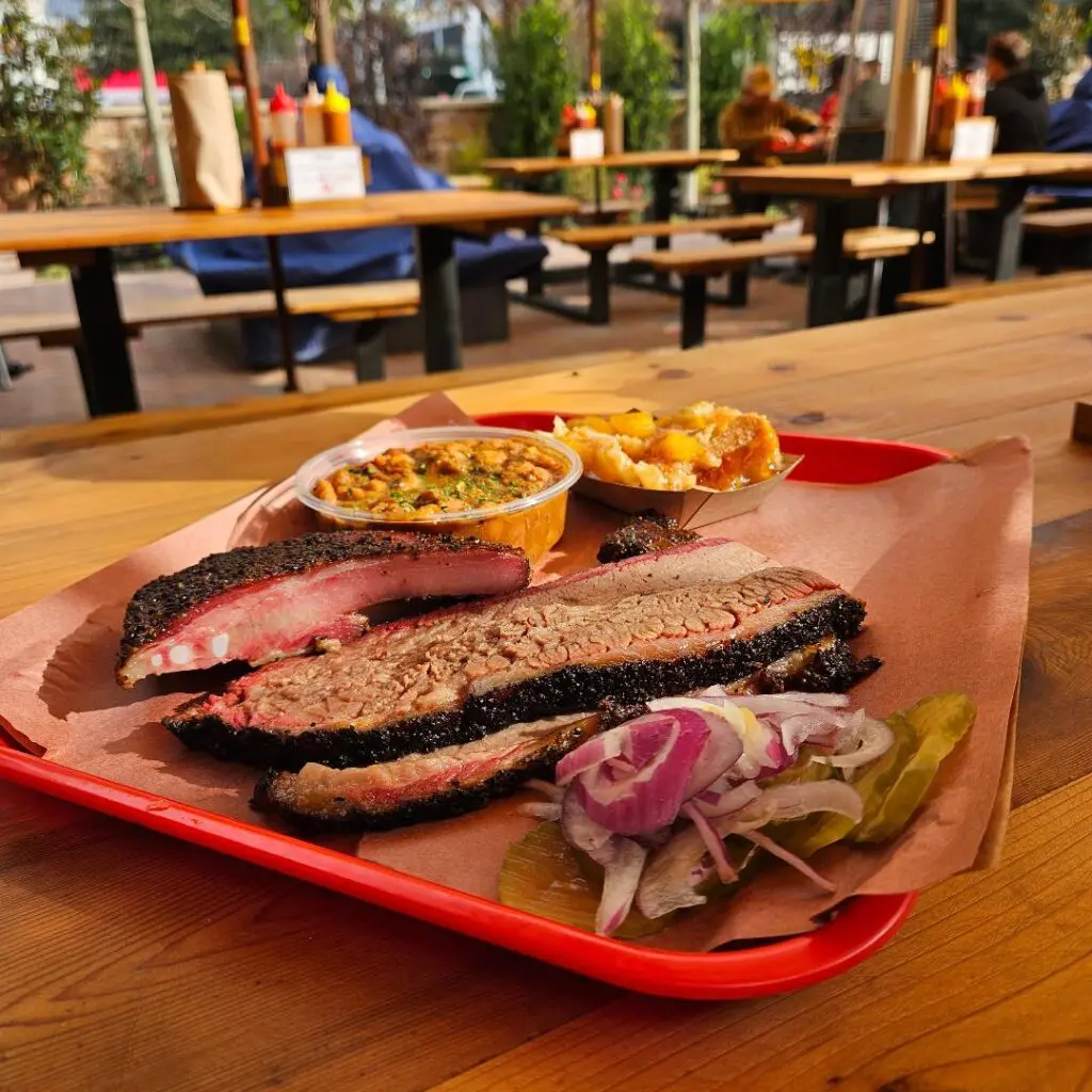 A mouthwatering spread from Terry Black’s Barbecue: tender brisket with a peppery bark, juicy pork ribs, brisket-laden pinto beans, and a rich peach cobbler with a buttery crust. (Photo by Edward Brown)