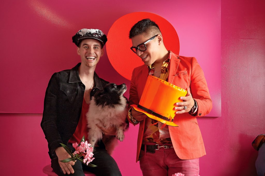 Joseph Steffen, holding his Pomeranian Cha Cha, wears a Dan & Joseph sequined police cap, $425. Dan Rodriguez, with a Dan & Joseph Day-Glo orange patent-leather top hat, $550. Artwork from Samantha McCurdy's "Snugs" series, $5,000.