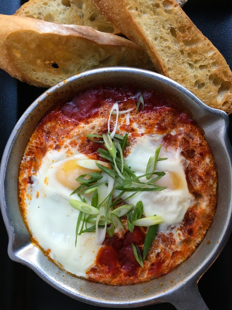 The General Public's Shakshuka, with crushed tomato, toasted cumin, and smoked paprika. Two soft-poached eggs sit atop with green onions for garnish and buttered baguette for dipping. (Photo courtesy Daniel Manchaca)