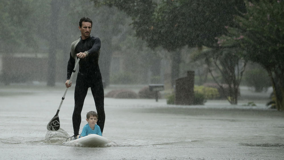 Alexendre Jorge evacuates four-year-old Ethan Colman from flooded neighborhood. (Photo by Charlie Riedel / AP)