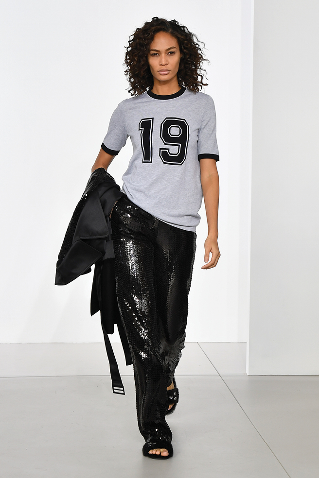 Michael Kors varsity T-shirt, black trousers, and black sequined coat.