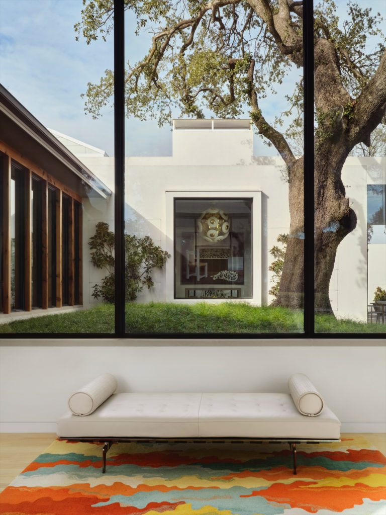 In the entry, Poltrona Frau bench from Scott + Cooner. Vintage rug. A long gallery at left connects an alcove in the family room, seen across the courtyard. The chandelier seen in the window is vintage Italian. (Photo by Lisa Petrole)