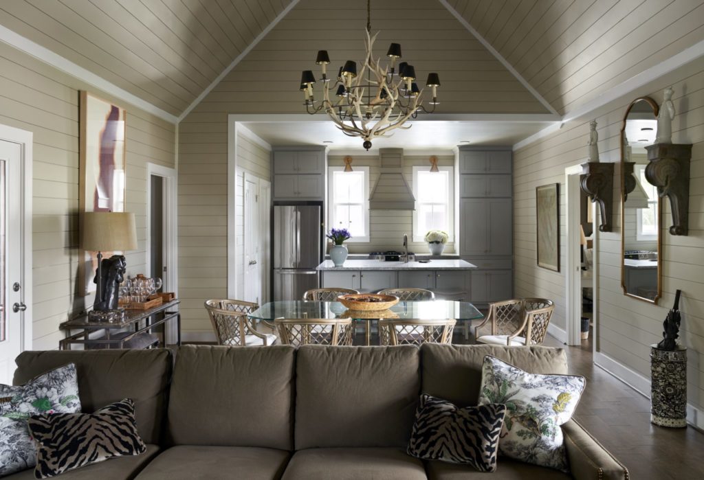 In a dining room in one of the bungalows, the antler chandelier is from JF Chen, Los Angeles. On the sofa, a pair of toile pillows embroidered by John Cone. Safavieh rattan dining chairs. Vintage Baldwin brass table from Memorial Traders, Houston. On wall, antique architectural elements and blanc de Chine statues along with bar cart are from Lewis & Maese Antiques and Auctions. Bronze lamp on bar cart is from Elizabeth Street Antiques, New York City. Liz Ward painting, Moody Gallery, Houston. (Photo by Pär Bengtsson)
