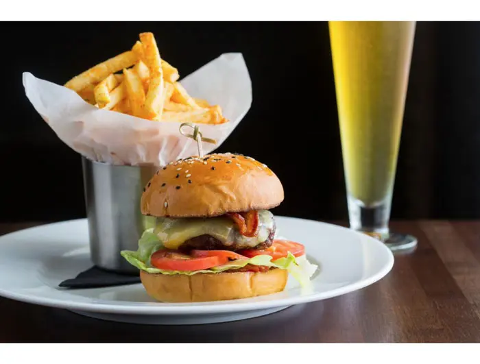 6-ounce Prime Bacon Cheeseburger at TABLE on Post Oak. 80/20 prime ground beef served with Applewood smoked bacon, 2-year aged white cheddar, tomatoes, house-made dill pickles, tomato jam, on a house=made sesame bun. 
