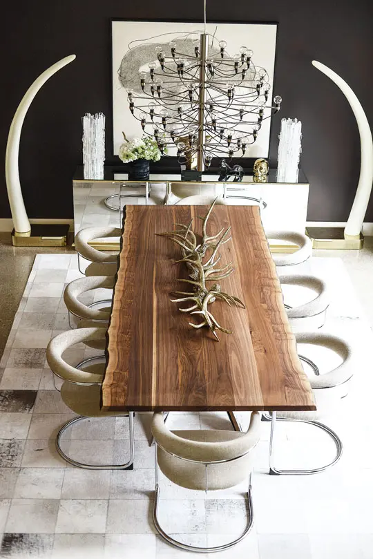 In the dining room, faux elephant tusks dramatically frame the walnut live-edge table, which is topped by a tangle of vintage faux antlers. Flos chandelier. Set of eight chrome Thonet dining chairs, sourced from Give & Take. Pearl Blocks cowhide rug from Neiman Marcus.