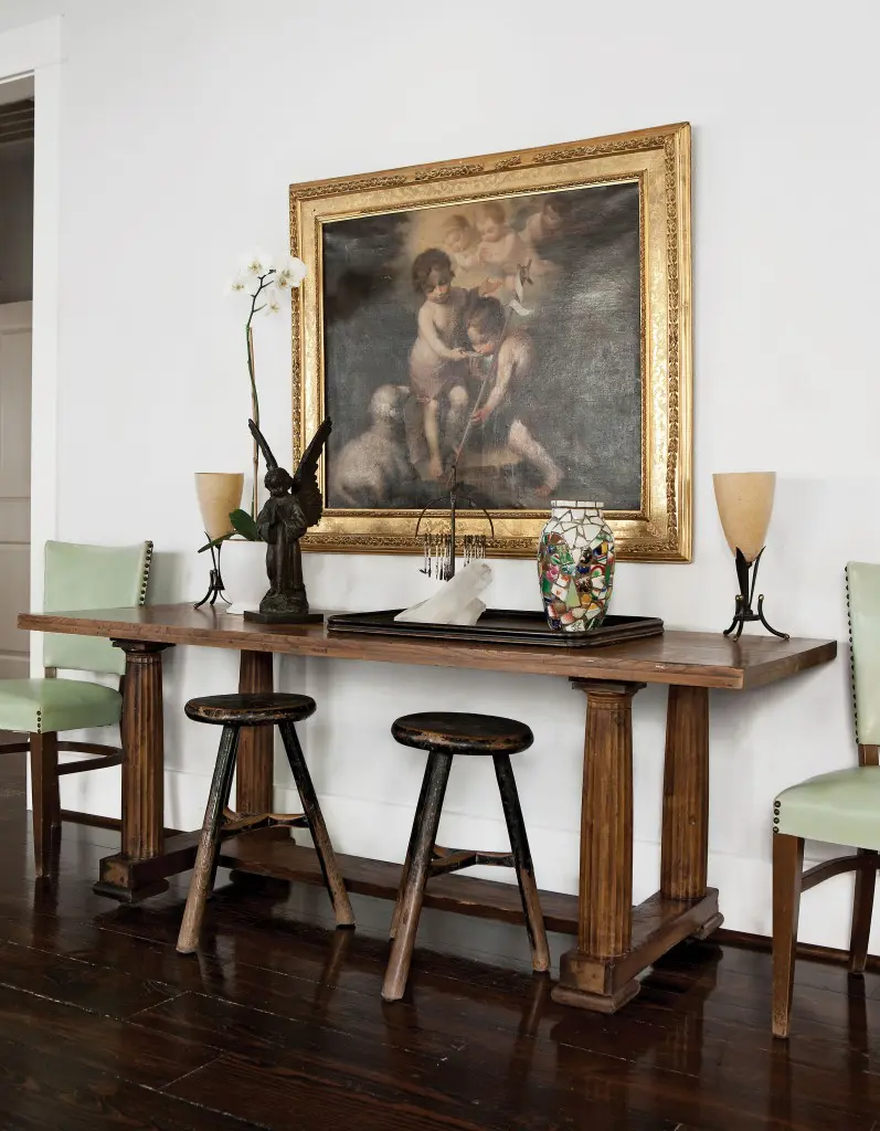 In the dining area, another beguiling mise en scène spans centuries, mixing a grand baroque canvas with a pair of humble stools. Hall table with classical columns gleaned from a
Heights antiquarian. The allegorical painting, a 19th-century reproduction of an earlier master, was literally rescued from a trash bin. Rustic stools from Kuhl-Linscomb, while the upright chairs came from the press room at the Rice Hotel, via an estate sale. Bronze angel from a Brazilian flea market. To its right, a macumba shrine, also from Brazil, where Cusack traveled to visit her mother in the 1980s.