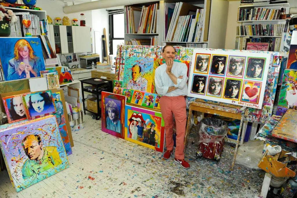 Simon Russell's photo of Peter Max in his studio, standing with portraits of celebrities and his interpretations of the Mona Lisa. 