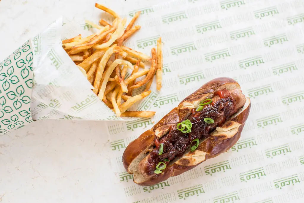 Rico's H-Town Dog — bacon-wrapped all-beef hot dog on a pretzel bun served with onion jam and ketchup.