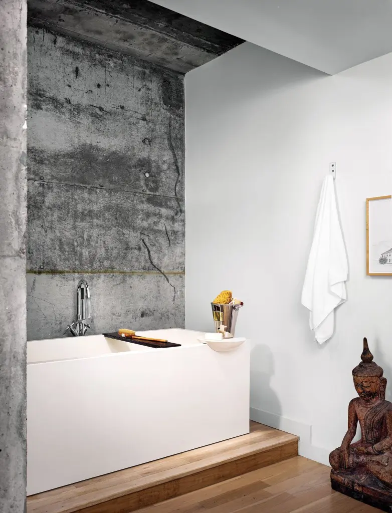 Wetstyle tub and antique Thai sculpture. Exposed-concrete wall.