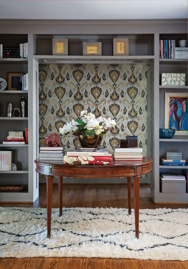Looke turned an awkward corridor into a statement hallway with Schumacher ikat wallpaper. The library is painted in Farrow & Ball Charleston Gray. The table, a family heirloom, pulls double duty with a leaf inserted and functions as an additional dining table for large dinner parties. 