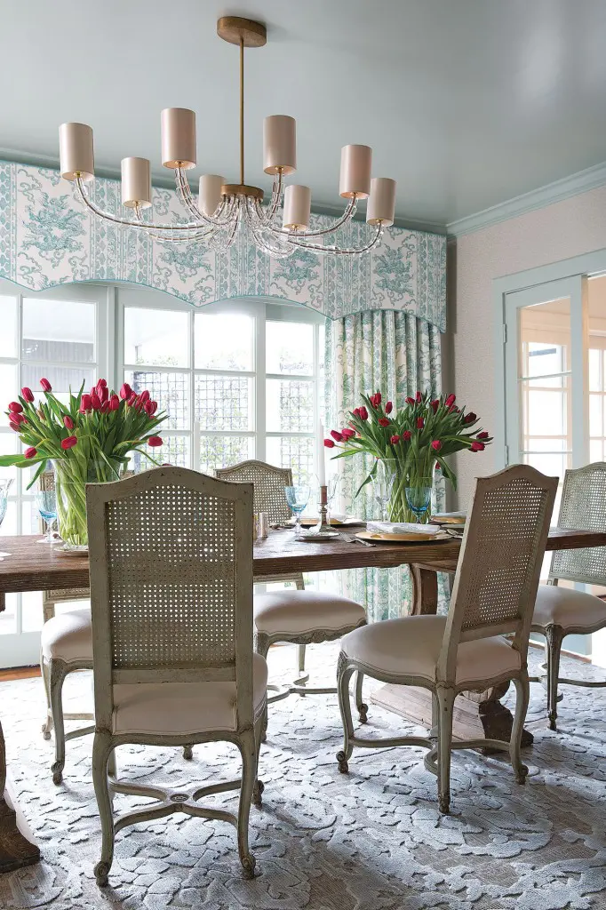The dining room is wallpapered in an aqua print from Lee Jofa. Ceiling and trim in Benjamin Moore Wythe Blue. Chandelier by Porto Romano. Curtains in Jim Thompson fabric frame the view of the backyard and pool. Louis XV dining chairs from Maison De Provence New Orleans surround an antique Italian table. Silk, cotton and jute rug from Carol Piper Rugs. 
