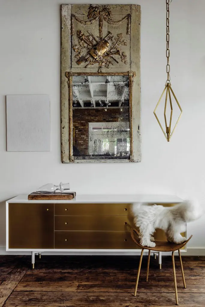 Brass-front and white lacquer credenza by Egg Collective. Louis XVI-period trumeau from South of France. Lily, Margaret Naeve’s
bichon-poodle mix, sits on a 20th-century Danish stool. Brass lantern circa 1970s. Cheryl Donegan, "Untitled (white leather)," 2013, through David Shelton Gallery.