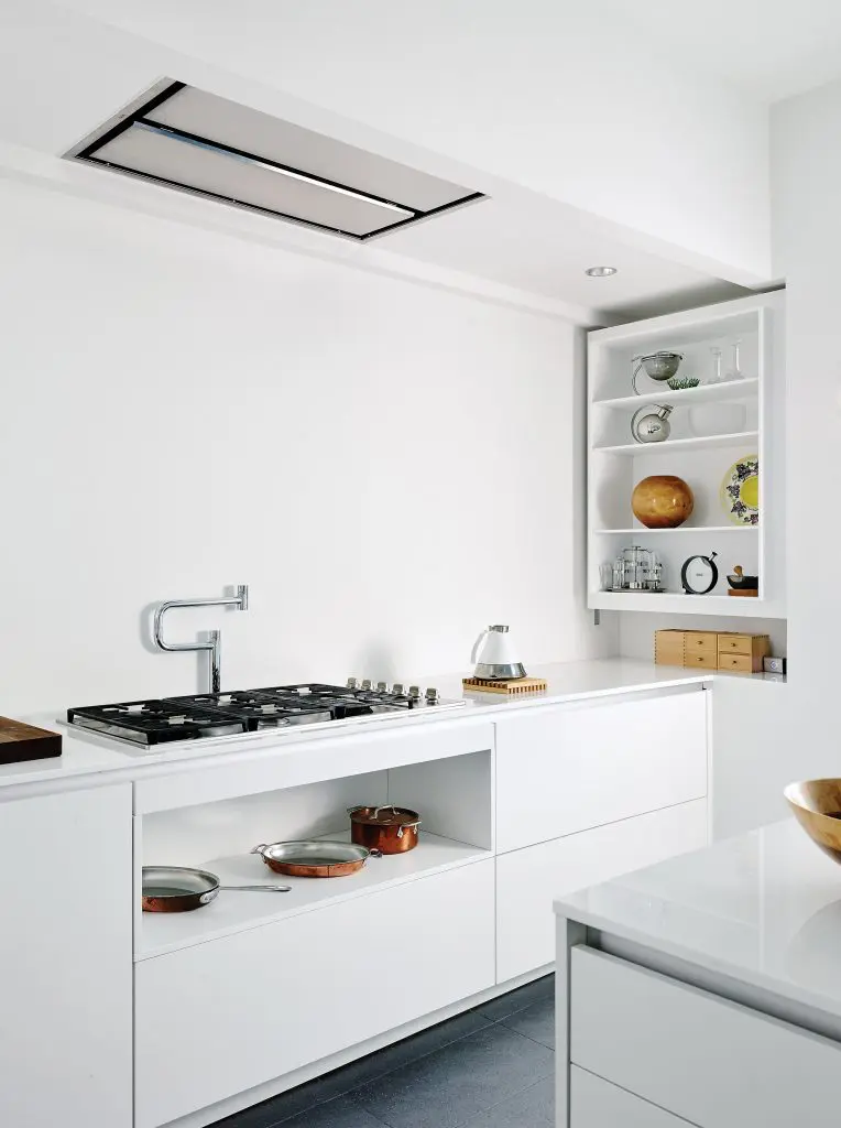 In the kitchen are Poggenpohl cabinets, custom white opaque glass countertops, Dornbracht plumbing fixtures. On the shelves, a collection of unique objects including a hand-turned wood vessel by Phillip Moulthrop and an Alessi Bauhaus martini shaker designed by Marianne Brandt. Tea kettle is an industrial design by Ross Lovegrove.