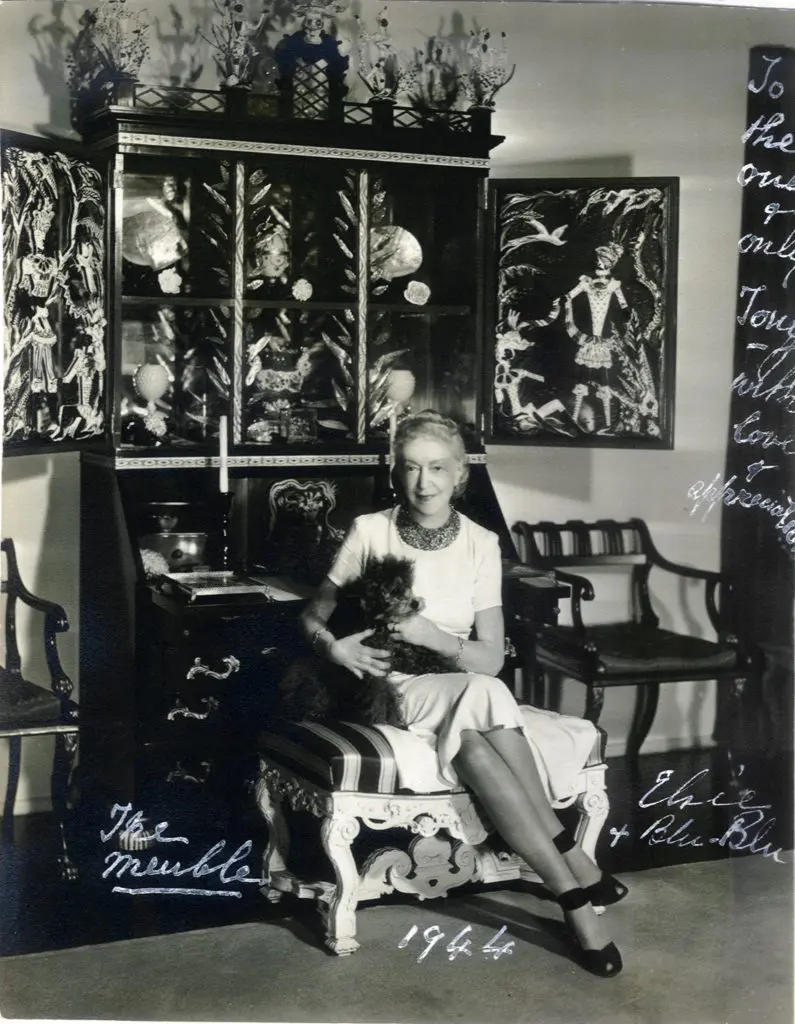 Elsie de Wolfe with Blu-Blu in front
of her meuble designed by Tony
Duquette, 1942