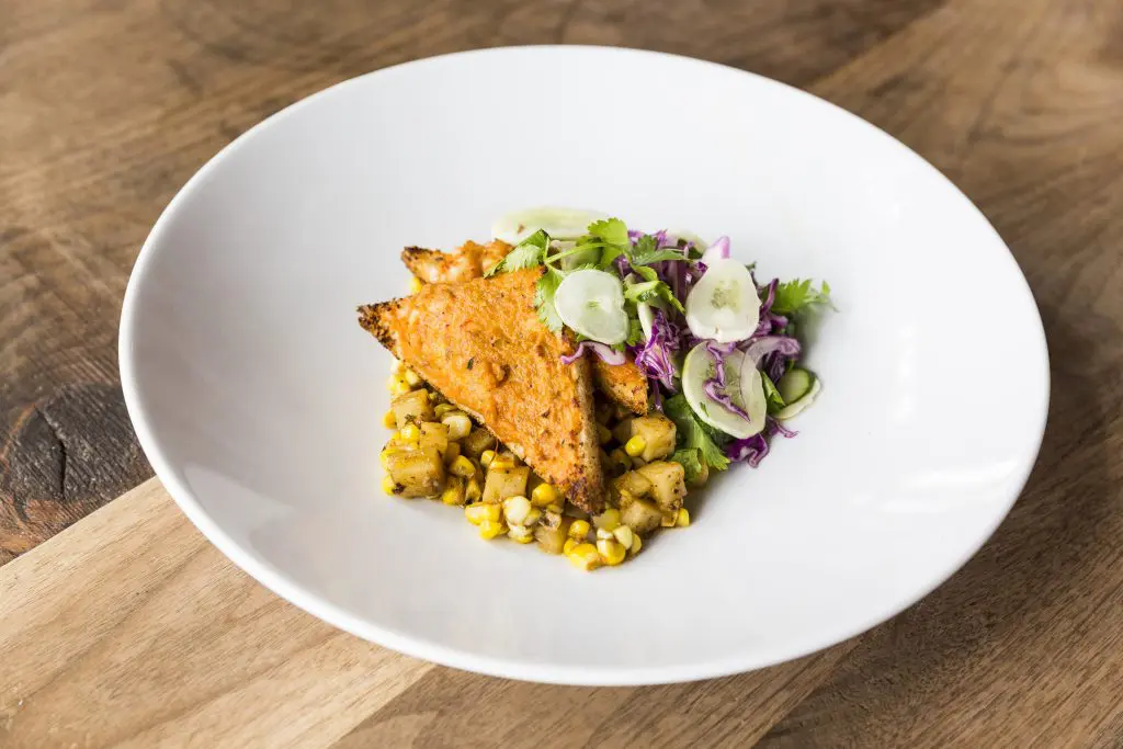 The Vietmanese-Style Crawfish Boil Toast is topped with corn, potatoes, and cucumber salad. 