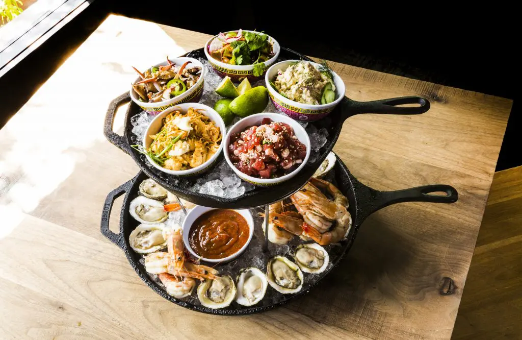 Underbelly's UB seafood tower is jam packed with Alabama oysters, Gulf shrimp, UB tamarind cocktail sauce, jalapeno lime mignonette, jumbo lump crab with chile mayonnaise, lime and crispy shallot; char siu tuna tartare, pickled lotus root, benne seed; garam masala smoked fish salad; dried chile lime marinated shrimp salad; and Nuoc cham marinated crab fingers, crushed peanuts, onions, and herbs. 