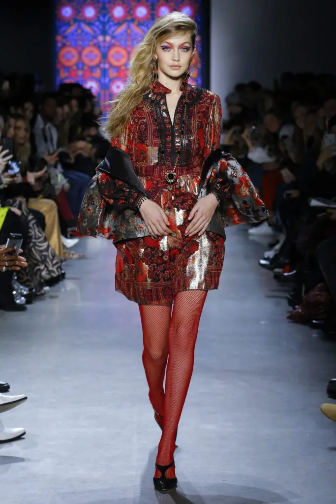 Model Gigi Hadid led off the Anna Sui fall 2018 runway show in a rouge multi-scattered flowers metallic brocade vest and multi-paisley blooms metallic dress.