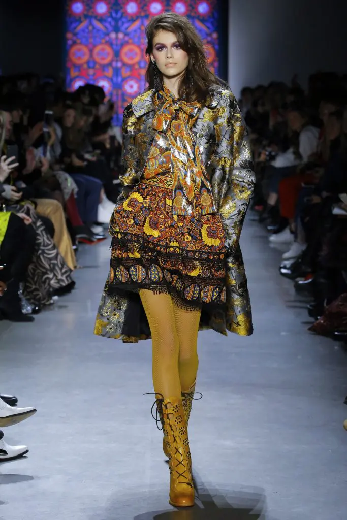 Kaia Gerber in Anna Sui  sunshine multi scattered  flowers metallic brocade coat, multi paisley bloom jacquard skirt and metallic jacquard top.