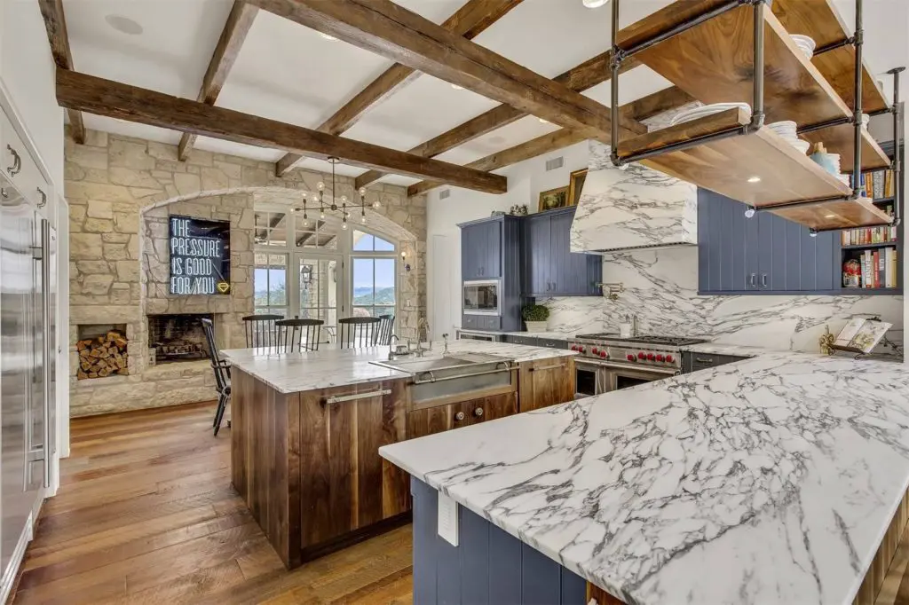 The redesigned kitchen features white marble countertops that contrast the exposed wood beams. 