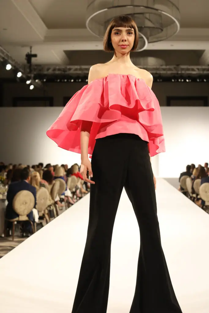 Carolina Herrera flamingo ruffled off-the-shoulder blouse and black bell bottom trousers. (Photo by Priscilla Dickson Photography)