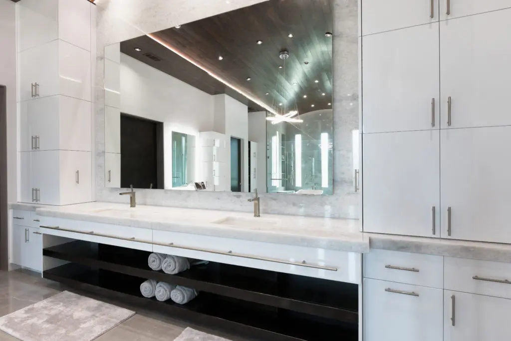 Double vanities with quartzite countertops are flanked by  white gloss frameless cabinets in the Frankel Building Group home.