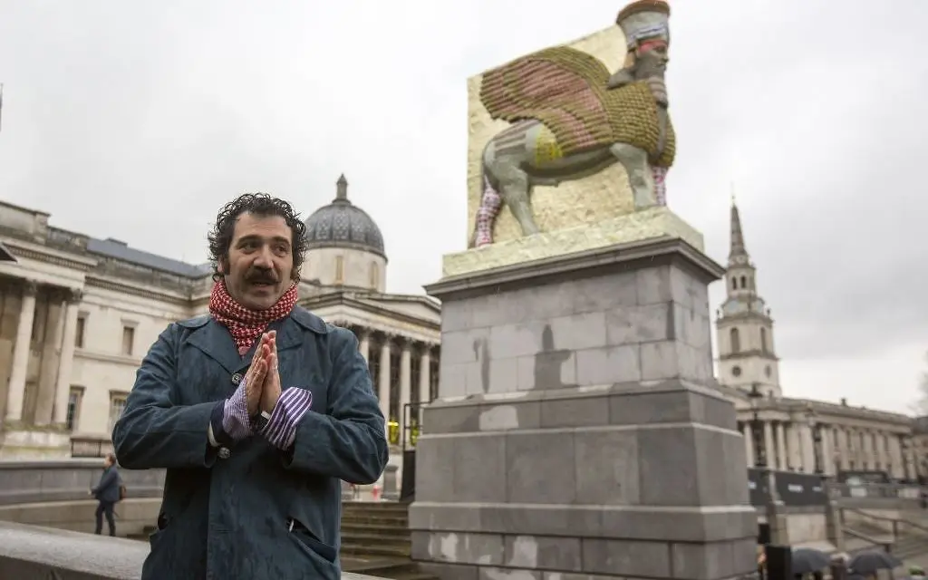 Michael Rakowitz stands with his work in London's Trafalgar Square, 2018, "The Invisible Enemy Should Not Exist." The human-headed figure of a winged bull (lamassu) is constructed from cans of Iraqi date-syrup, a staple of the region's cuisine. (Photo Rick Findler/PA Wire, courtesy Jewish News Times of Israel)