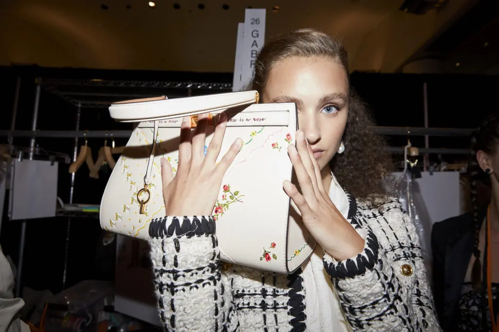 Backstage, a model in a Tory Burch linen and tweed jacket, showcases a handbag with a stitched floral pattern. (Photo courtesy of Tory Burch)