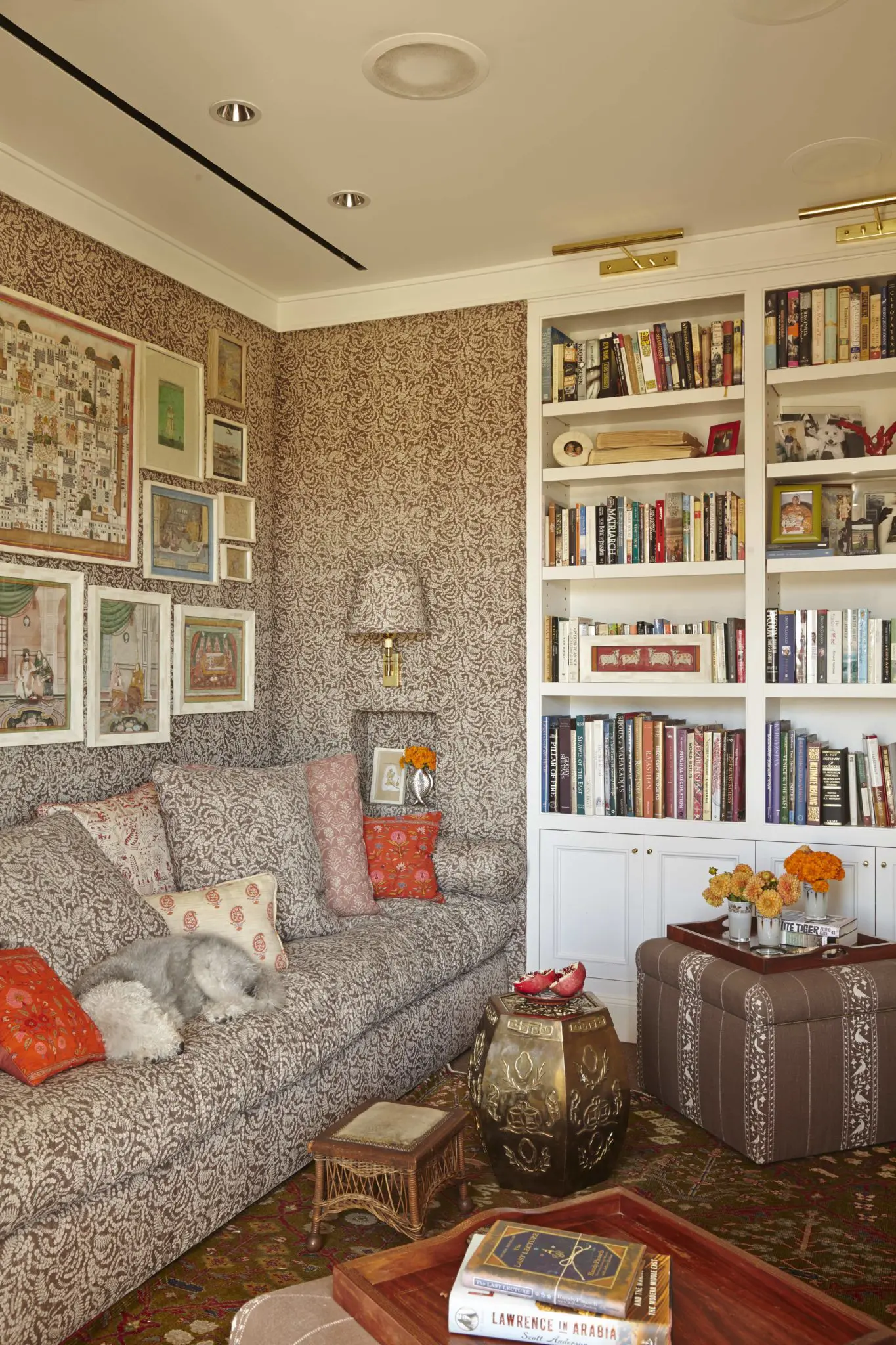 In the TV room, Fine's collection of Indian miniatures and portraits framed in camel bone, discovered in New Delhi. Lisa Fine Textiles Malula covers the walls, sofa, and sconce shade. GoGo, a Bedlington terrier, sleeps on the sofa. the agra rug from Abrash Rug Gallery. ceramic stool from Ceylon et Cie.