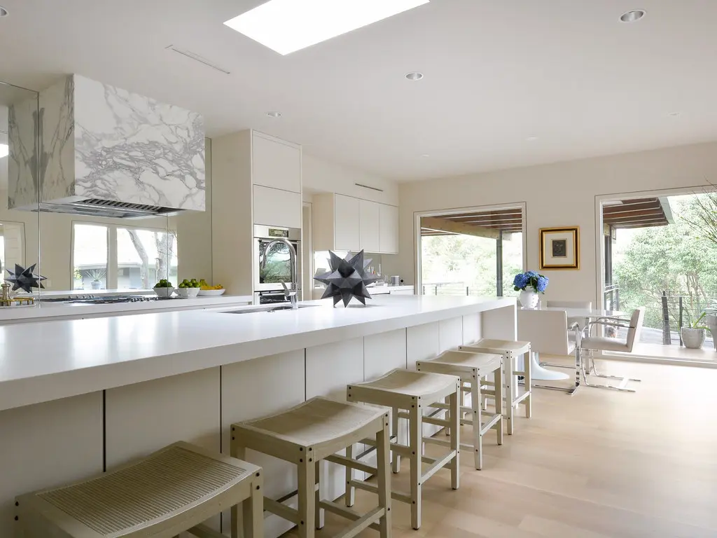 Honed white Caesarstone countertops and white Palecek barstools provide a sleek look to the remodeled kitchen.
