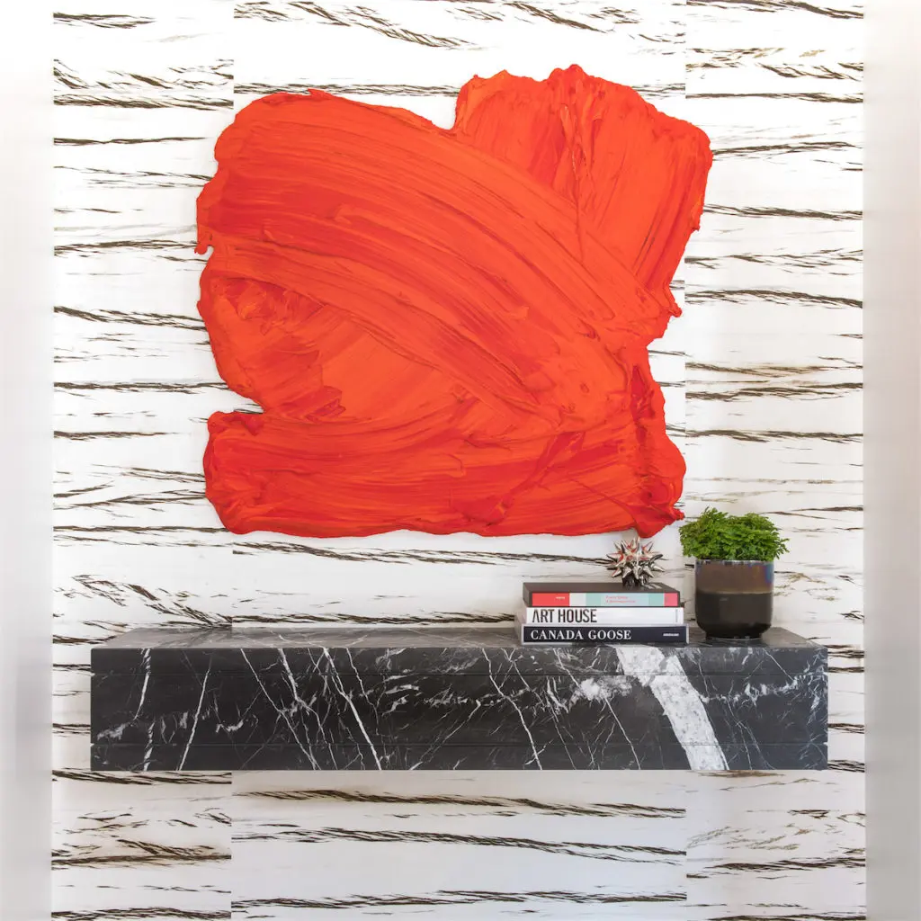 The vivid red swoosh of Donald Martiny's "Maek" from Galleri Urbane provides just the right punch at the entry. A black Holland Marble shelf sets off the graphic lines in the Élitis wallpaper from George Camerson Nash. (Photo by Costa Christ Media)