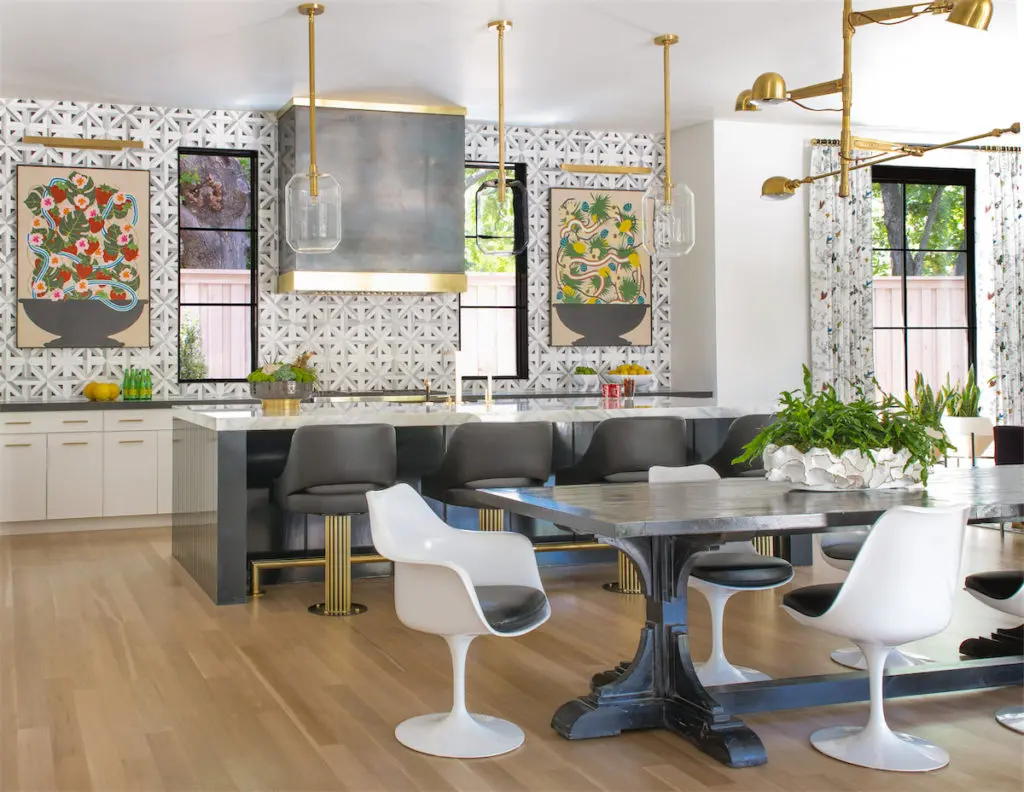 To enhance the kitchen's bistro look, the family's farmhouse table was stained black and paired with Knoll Saarinen chairs upholstered in black leather. Upper cabinets were eliminated in favor of graphic tile and artwork by Stephen D'Onofrio from Galleri Urbane. Ralph Lauren lighting. (Photo by Costa Christ Media)