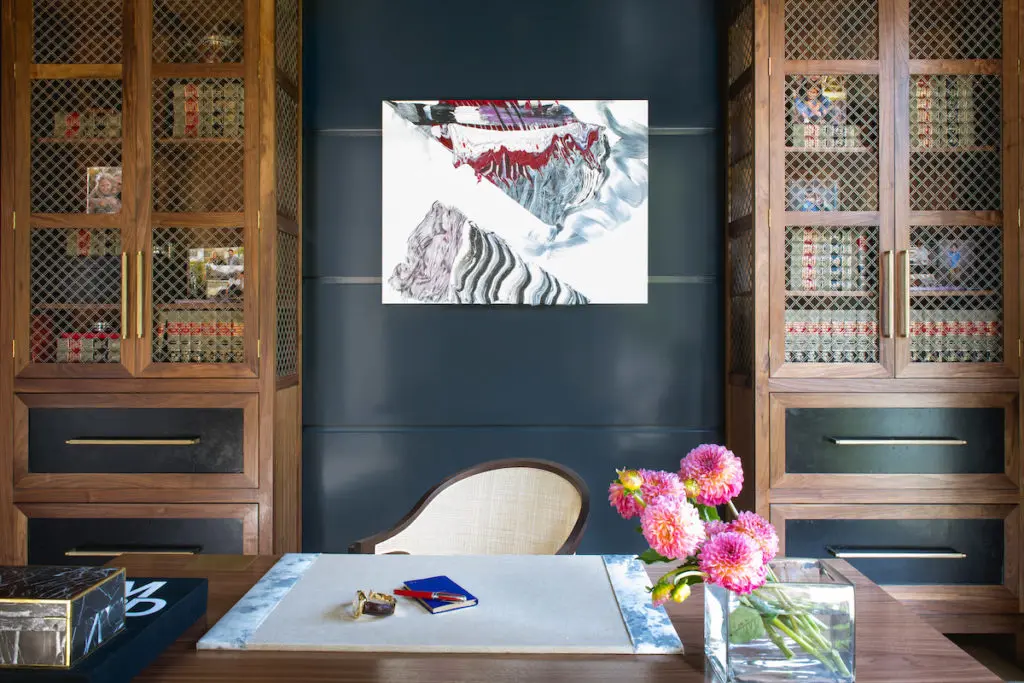 Designer Philip Thomas Vanderford gives the study a clubby feel with rich custom walnut-and-brass bookcase towers and desk, and creamy leather chairs by Edward Wormley for Baker and Eames. The dark, high-gloss ceiling and walls add reflected light; the Kelly Wearstler side table from Allan Knight and hand-knotted Abrash rug lend texture. Ralph Lauren for Visual Comfort light fixture. Antique terra-cotta garden-ball sculpture. (Photo by Costa Christ Media)