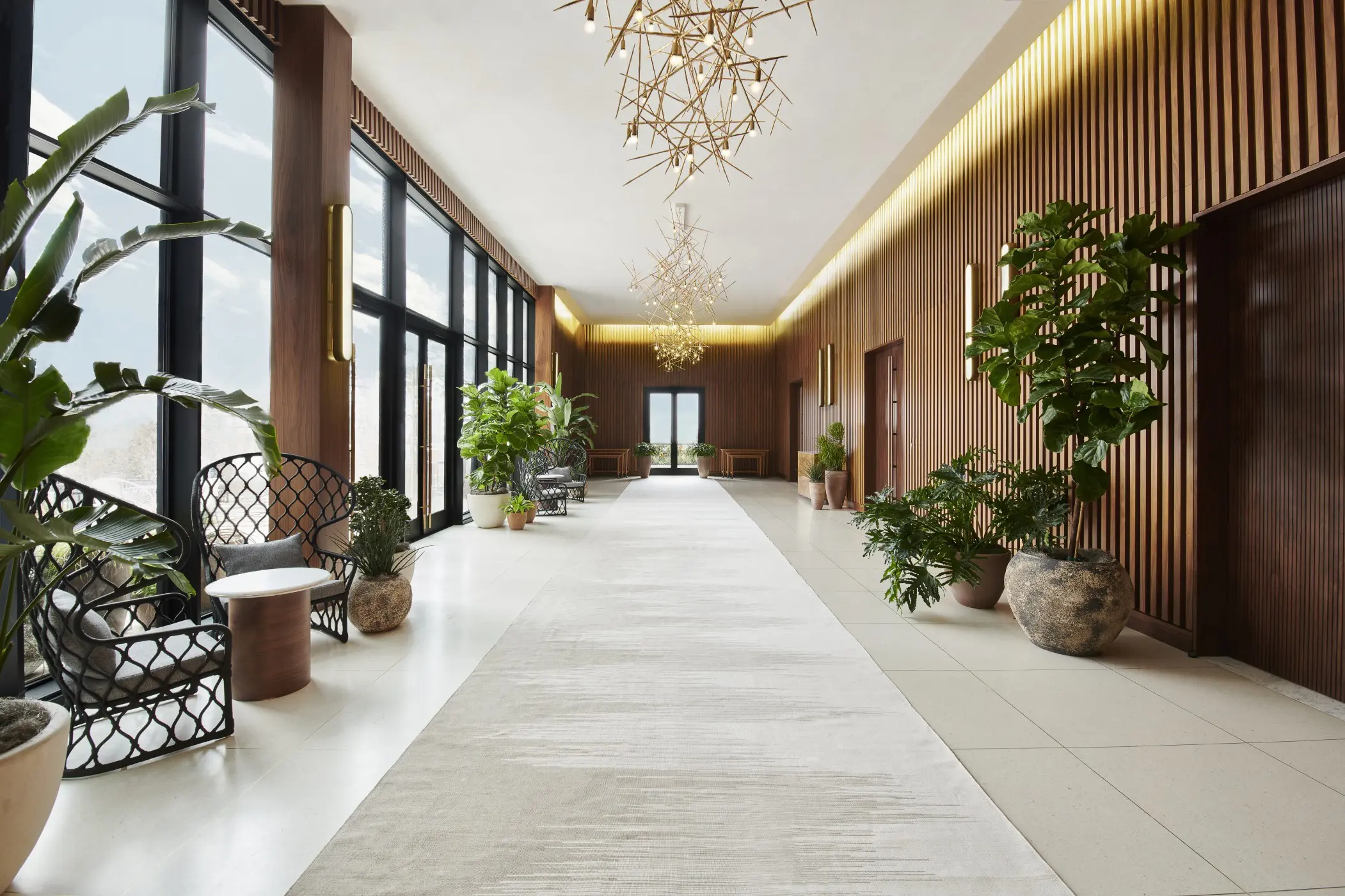 Swoon's glam-meets-earthy design leading to the hotel's meeting rooms includes rattan furniture, rustic pottery, plants, wood paneling, custom brass light pendants, and elegant custom runner.
