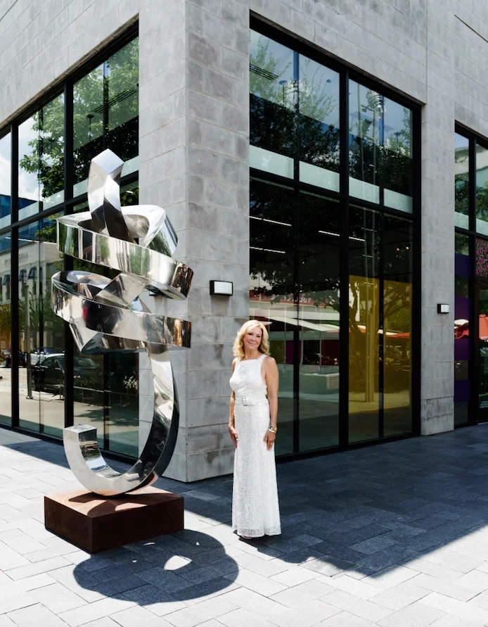 Laura Rathe at the entrance to her new River Oaks District space, unveiling Thursday, October 1. Rathe, who marked her 20th anniversary as a gallerist in 2019, will now have three Texas spaces: her original gallery on Colquitt, a Dallas location in the Design District, and now this high-profile site at River Oaks District. The gallerist stands next to Gino Miles’ stainless-steel sculpture “Omen,” 2019. (Photo by Jack Thompson)