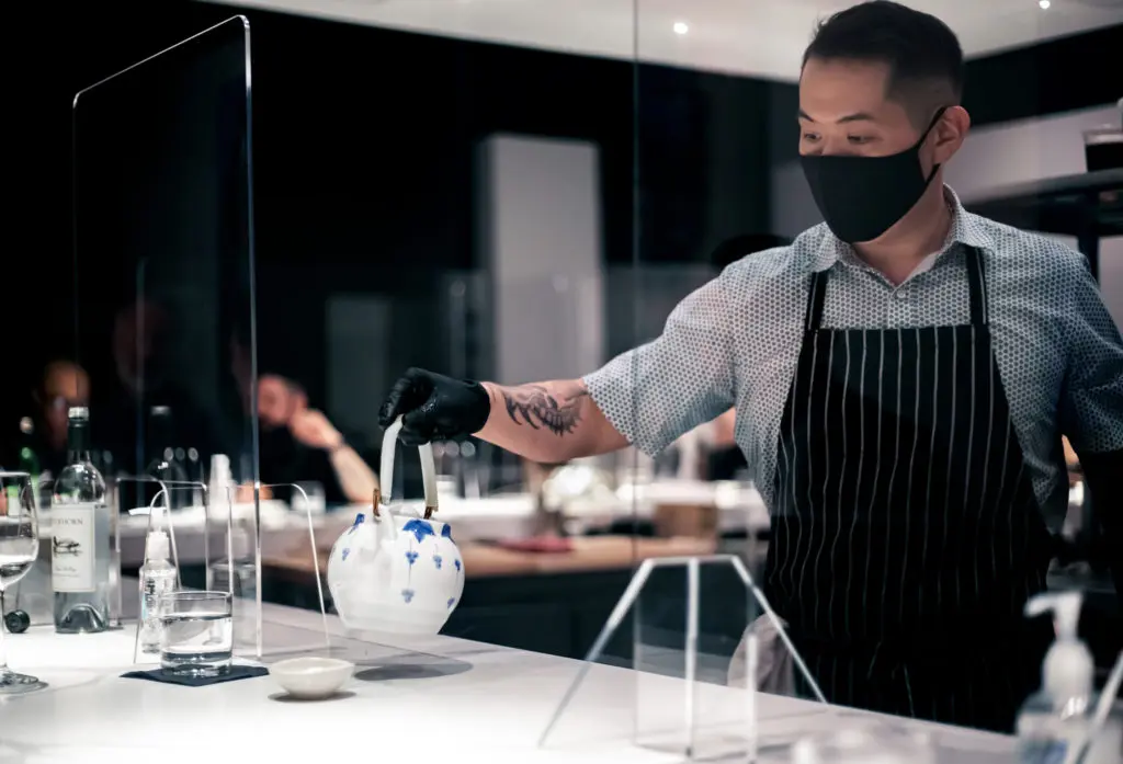 Hidden Omakase chef Billy Kin pours tea for a diner in a socially-distanced dining area. (Photo by Katoe Productions)