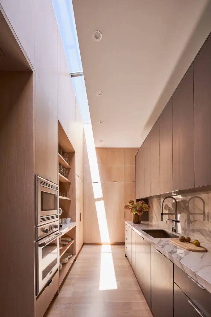 In the prep kitchen, a ribbon of light from the skylight travels like a sundial. White oak cabinets and floors. Sintered-stone countertops. (Photo by Stephen Karlisch)