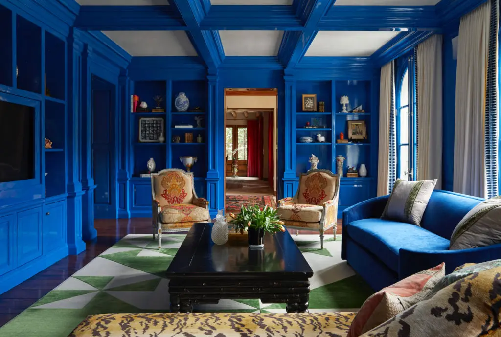 The library is painted a custom blue by Benjamin Moore. Custom rug through James showroom. Cuellar Custom Upholstery fabricated the chaise, covered in Scalamandré
velvet, and the sofa, covered in Pierre Frey mohair. Vintage chairs upholstered in Schumacher embroidered fabric. Brass palm-tree floor lamps from Europe. (Photo by Pär Bengtsson)