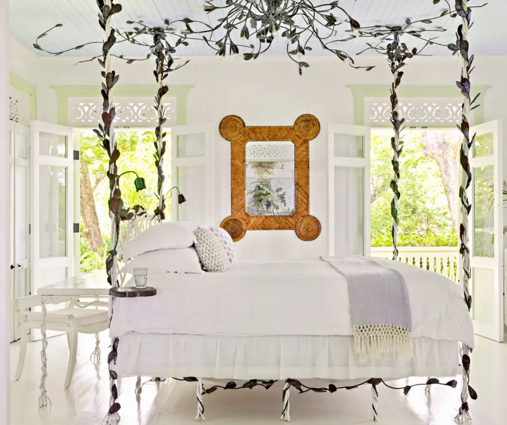 The master bedroom in Celerie's bungalow with an iron bed reminiscent of the one she had as a child, but this one has tiny lights tucked into the leaves. Small reading lamps shaped like tulips hang over the headboard, and bedside tables are swiveling lily pads. 