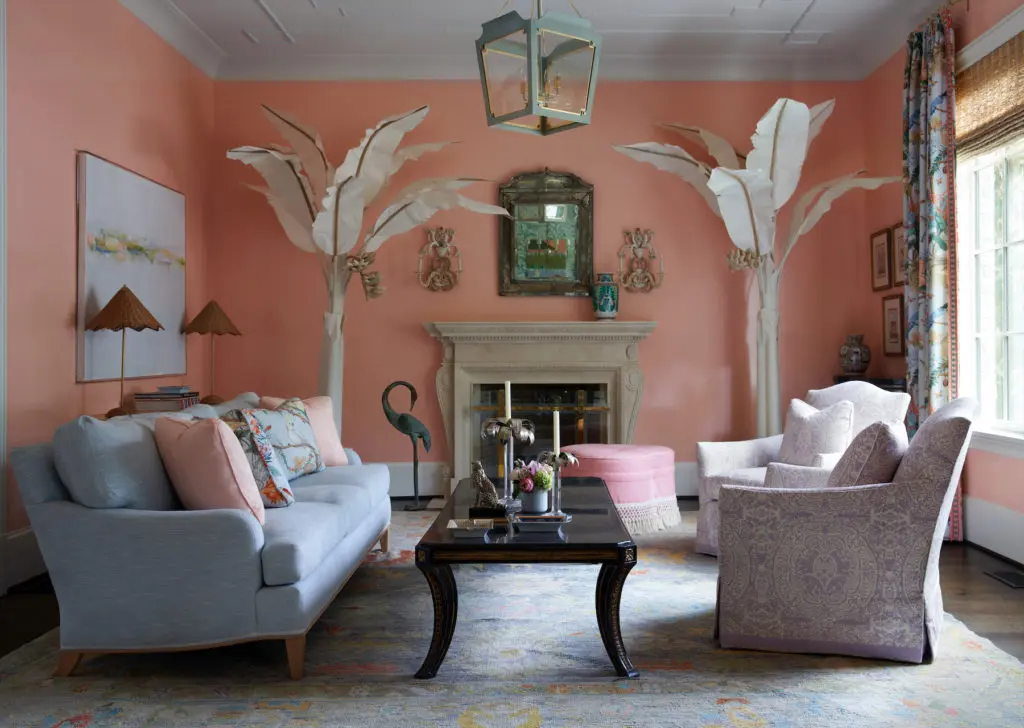 The formal living room’s coral walls are painted a custom Benjamin Moore color. Canvas-and-wood palm trees were the homeowner’s find. Scalamandré draperies. Chairs in Quadrille fabric. Madre ottoman in Pierre Frey fabric. Lee Industry sofa in Thibaut fabric. Visual Comfort lantern. Vintage shell sconces. Antique Venetian mirror. (Photo by Pär Bengtsson)