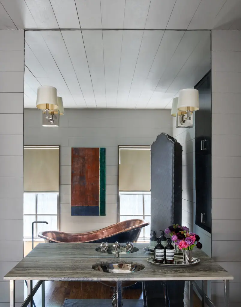 As reflected in the mirror, RH sconces, Waterworks fittings, silver travertine countertop. Pine paneling in Pratt & Lambert Old Silver. Paul Storr tray, 1821. (Photo by Pär Bengtsson)