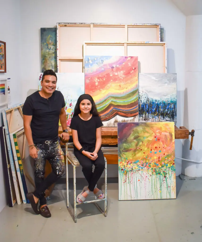 Melinda Moreno seated next to Edgar Medina and their opulent canvas, "Summer," 2021.
