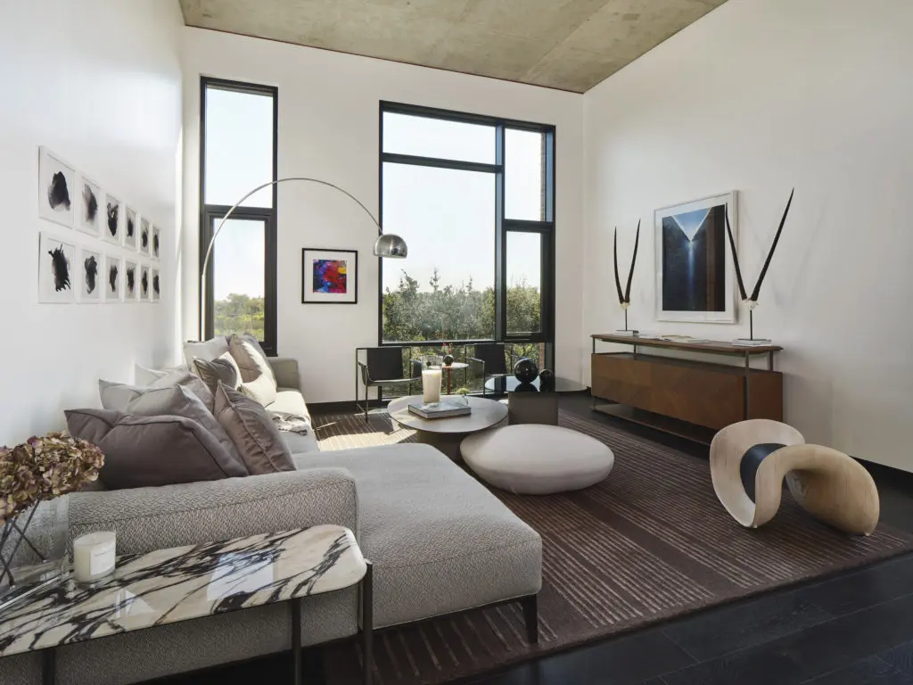 Giorgetti sofa, sideboard, coffee tables and poufs, marble side table, area rug and accent stool.  Poltrona Frau armchairs with wood side table and Flos Floor Lamp.  John David Robbins “Smokes 1-12” series (above sofa), Tyler Shields “RGB” (next to windows) and Caleb Charland “Pouring Light” (above sideboard) artworks. (Photography by Andrea Calo)