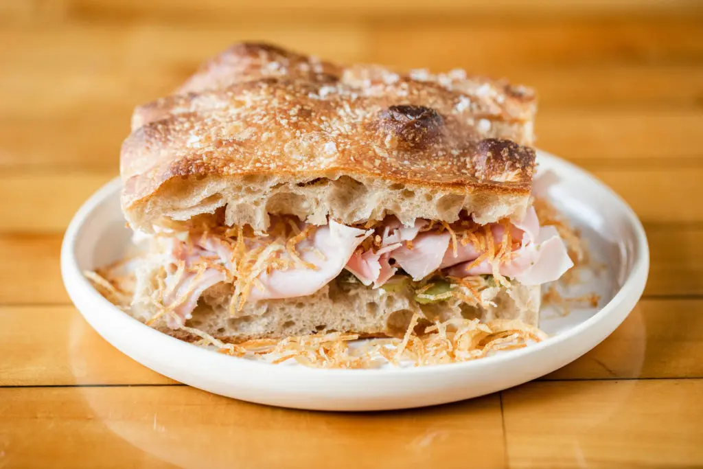 The popular Ham "Sammich" is made with house-baked focaccia bread, French ham, tater tot strips, and a cornichon relish. (Photo by Becca Wright)