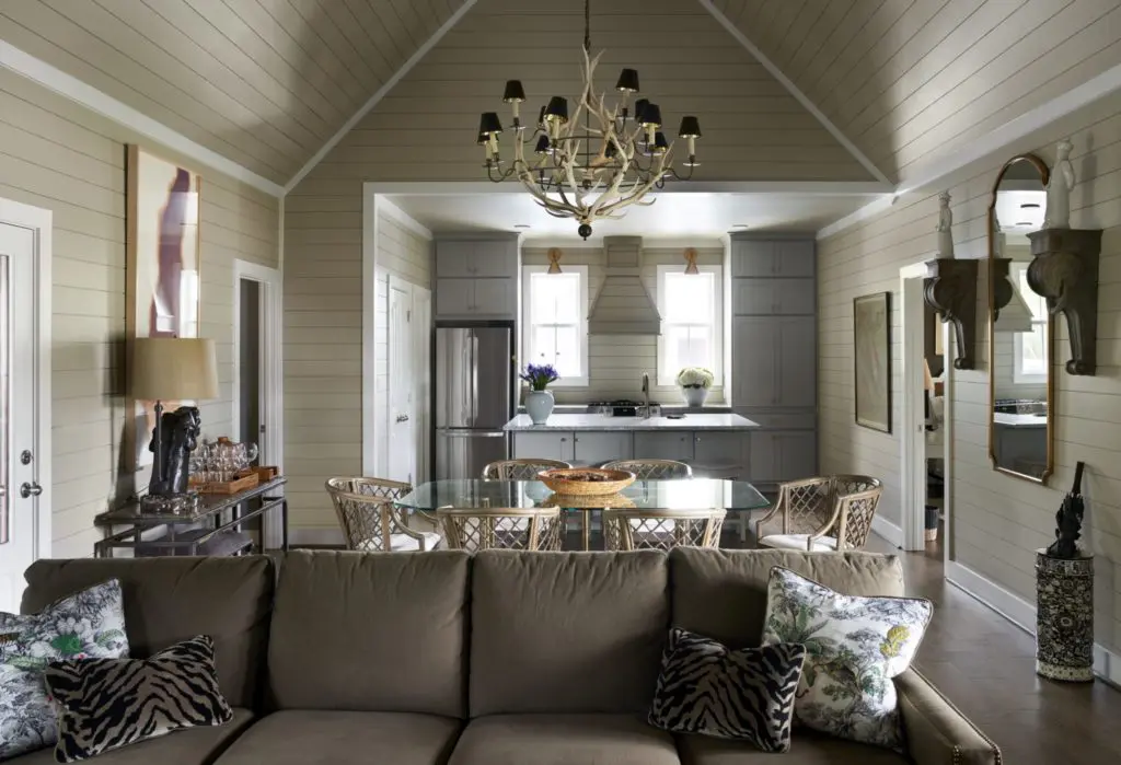 In a dining room in one of the bungalows, the antler chandelier is from JF Chen, Los Angeles. On the sofa, a pair of toile pillows embroidered by John Cone. Safavieh rattan dining chairs. Vintage Baldwin brass table from Memorial Traders, Houston. On wall, antique architectural elements and blanc de Chine statues along with bar cart are from Lewis & Maese Antiques and Auctions. Bronze lamp on bar cart is from Elizabeth Street Antiques, New York City. Liz Ward painting, Moody Gallery, Houston. (Photo by Pär Bengtsson)