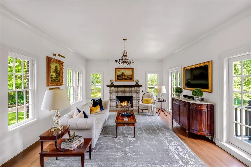A window-lined formal living features an elegant (and highly valuable) Rookwood tile fireplace.